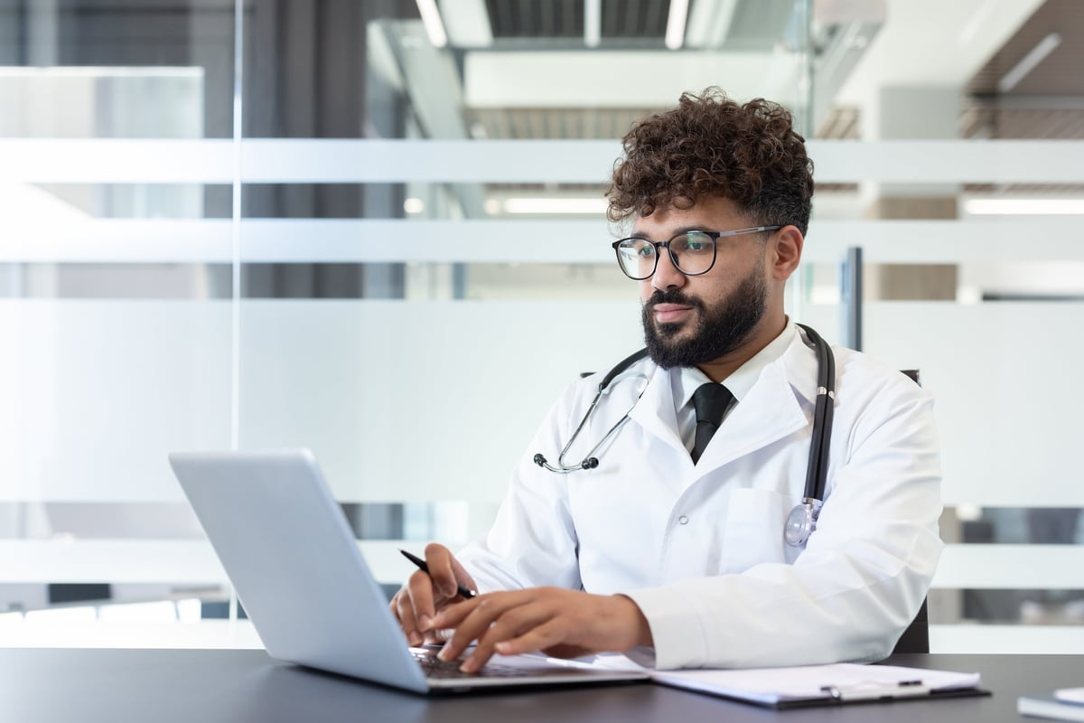 Young male doctor working on a laptop, providing online consultations and managing patient records in a contemporary medical office