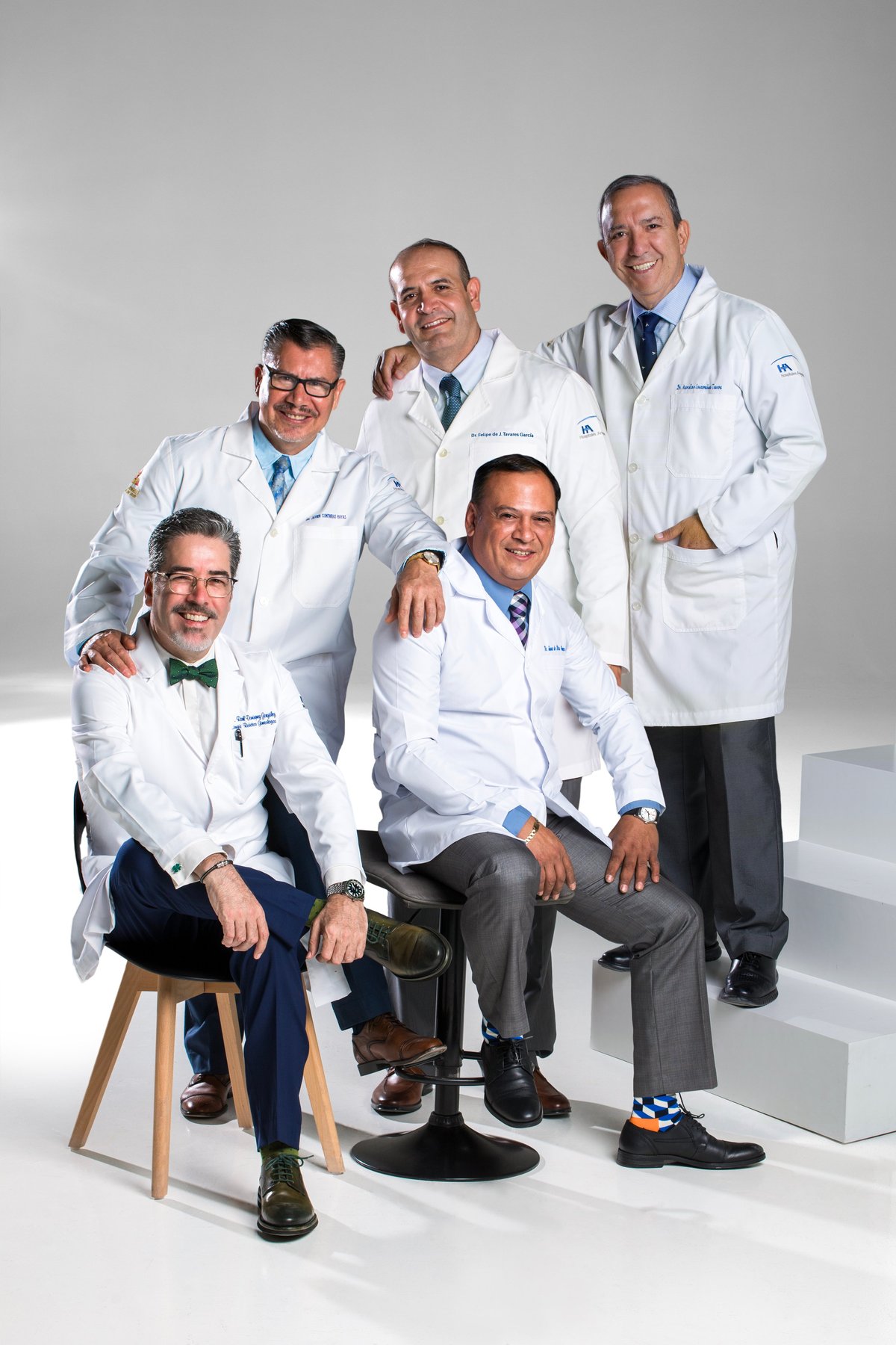 Five male doctors in white lab coats and blue shirts posing together against a white background in a professional team portrait